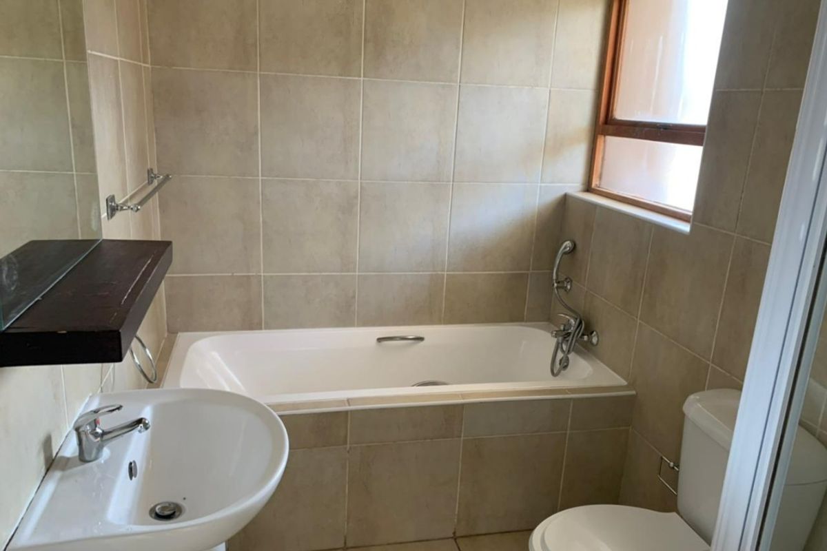 A functional bathroom featuring a built-in bathtub, pedestal washbasin, and toilet, finished with neutral wall and floor tiling.