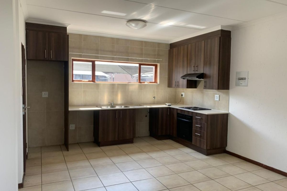 A functional, empty kitchen featuring dark wood cabinetry, tiled backsplash, built-in oven, hob, and extractor fan with neutral floor tiles.