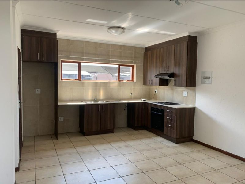 A functional, empty kitchen featuring dark wood cabinetry, tiled backsplash, built-in oven, hob, and extractor fan with neutral floor tiles.