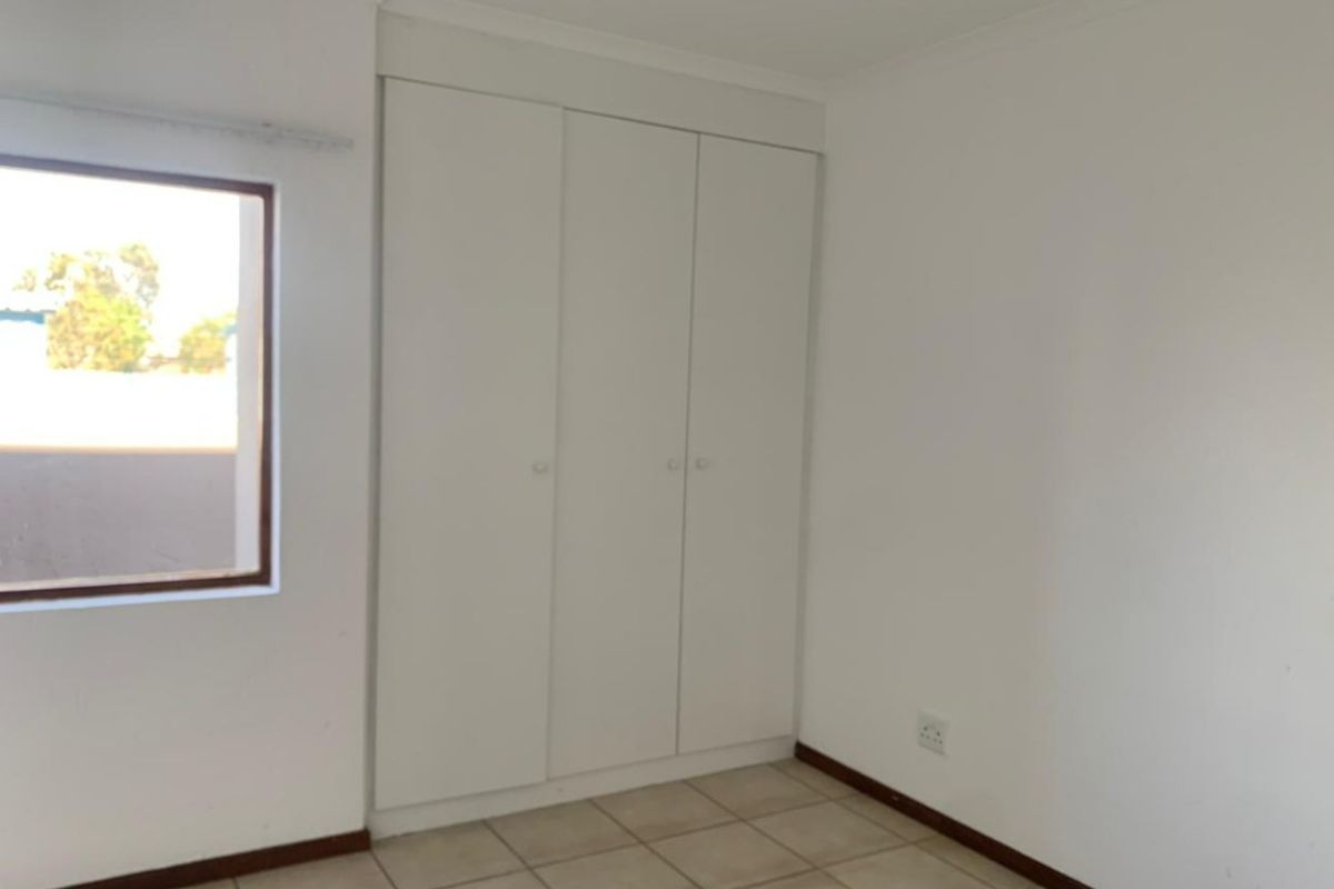 A clean, empty bedroom featuring neutral tiled flooring and a built-in white wardrobe, offering a blank canvas for personalization.