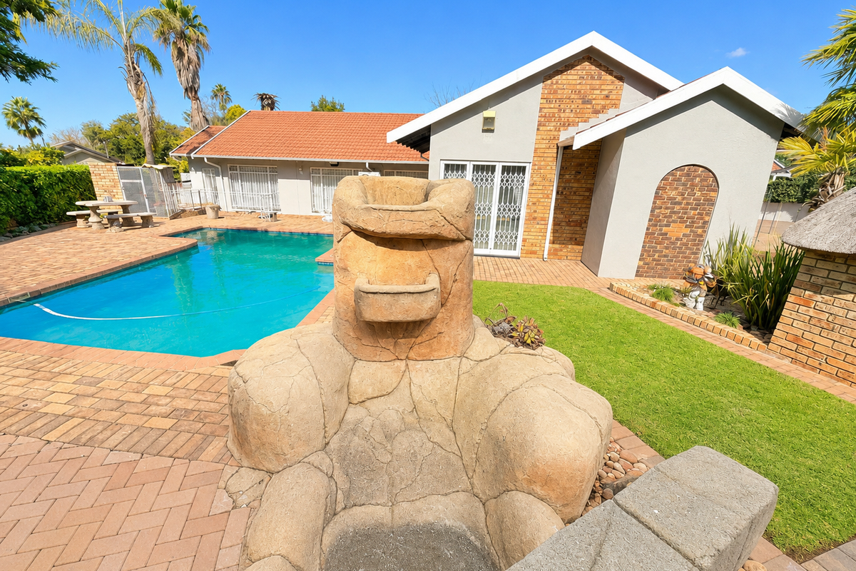 A well-maintained rear garden featuring a swimming pool, paved patio area, and a decorative stone-look water feature or fire pit.