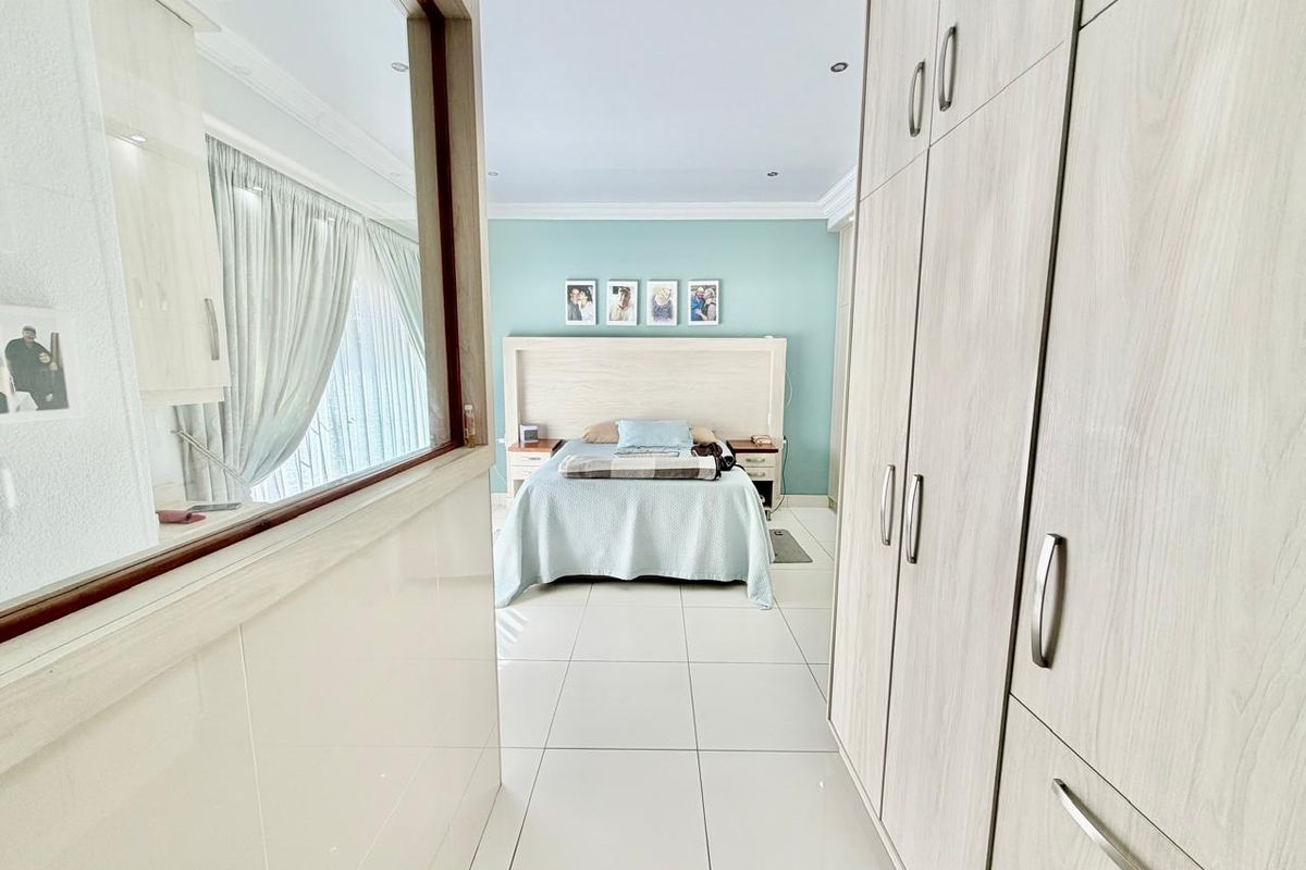 A well-maintained bedroom featuring light-toned built-in cupboards, tiled flooring, recessed lighting, and a feature wall with a built-in headboard.