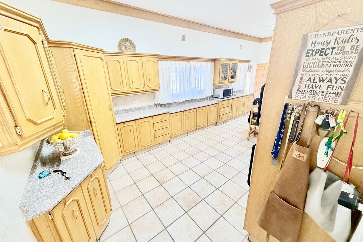 Spacious kitchen featuring extensive light wood cabinetry, granite countertops, and neutral ceramic floor tiles, offering ample storage and workspace.