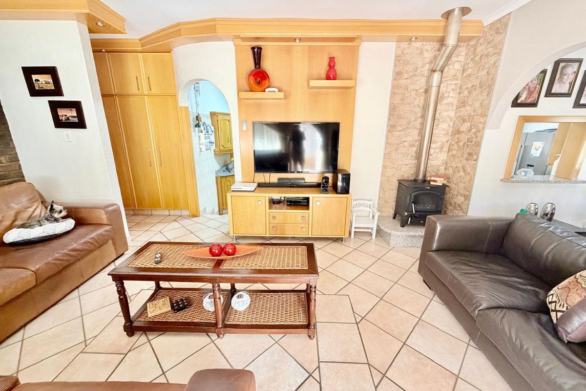 Spacious living room featuring a wood-burning stove, stone feature wall, built-in cabinetry, and tiled flooring, offering a cozy and functional living space.