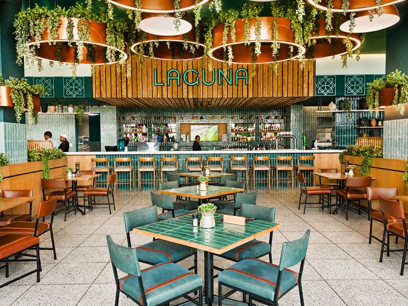 A modern, well-appointed bar area featuring a tiled counter, decorative timber slat wall paneling, and stylish circular pendant lighting with integrated greenery.