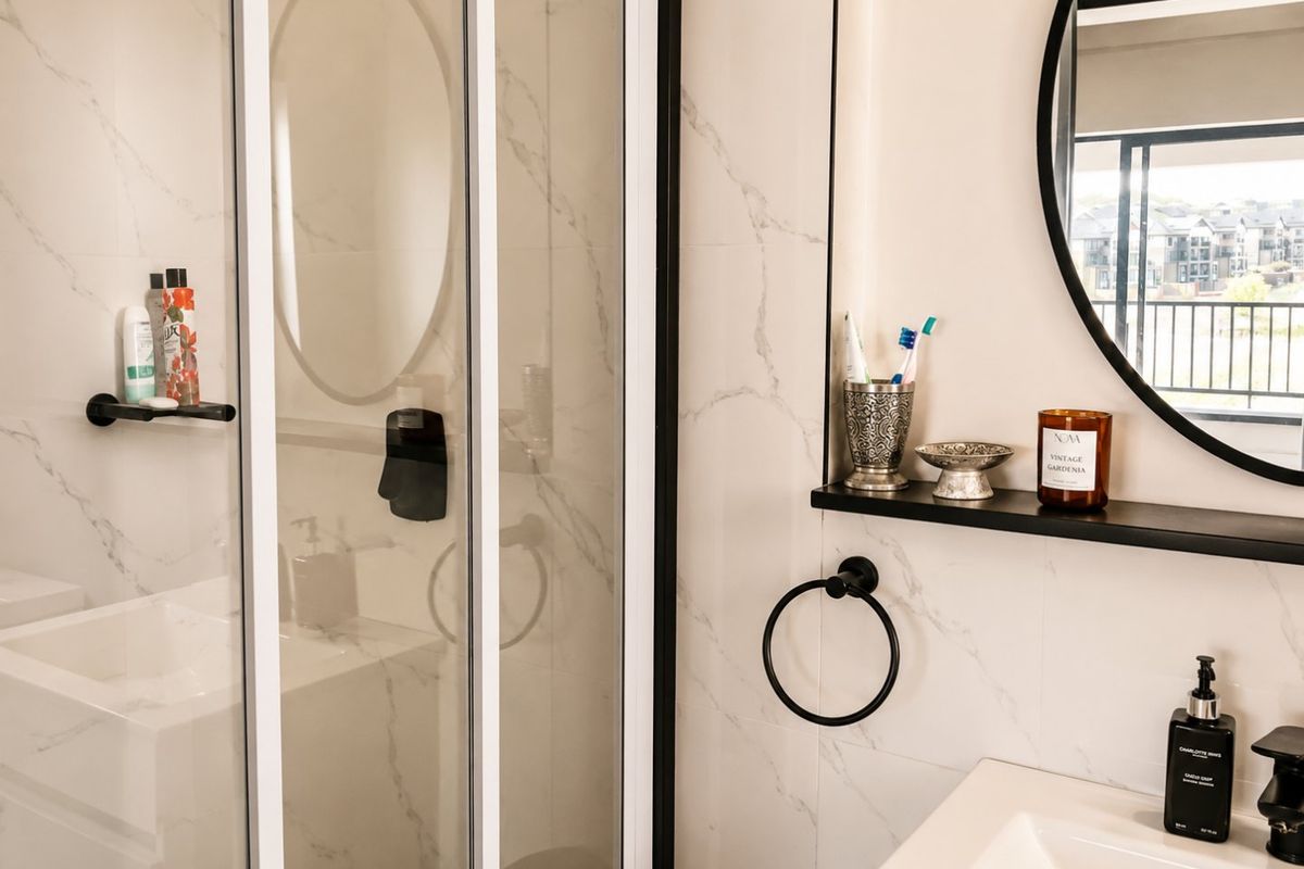 Modern bathroom featuring marble-look wall tiles, a walk-in shower with black frame, vanity basin, and contemporary black fixtures.