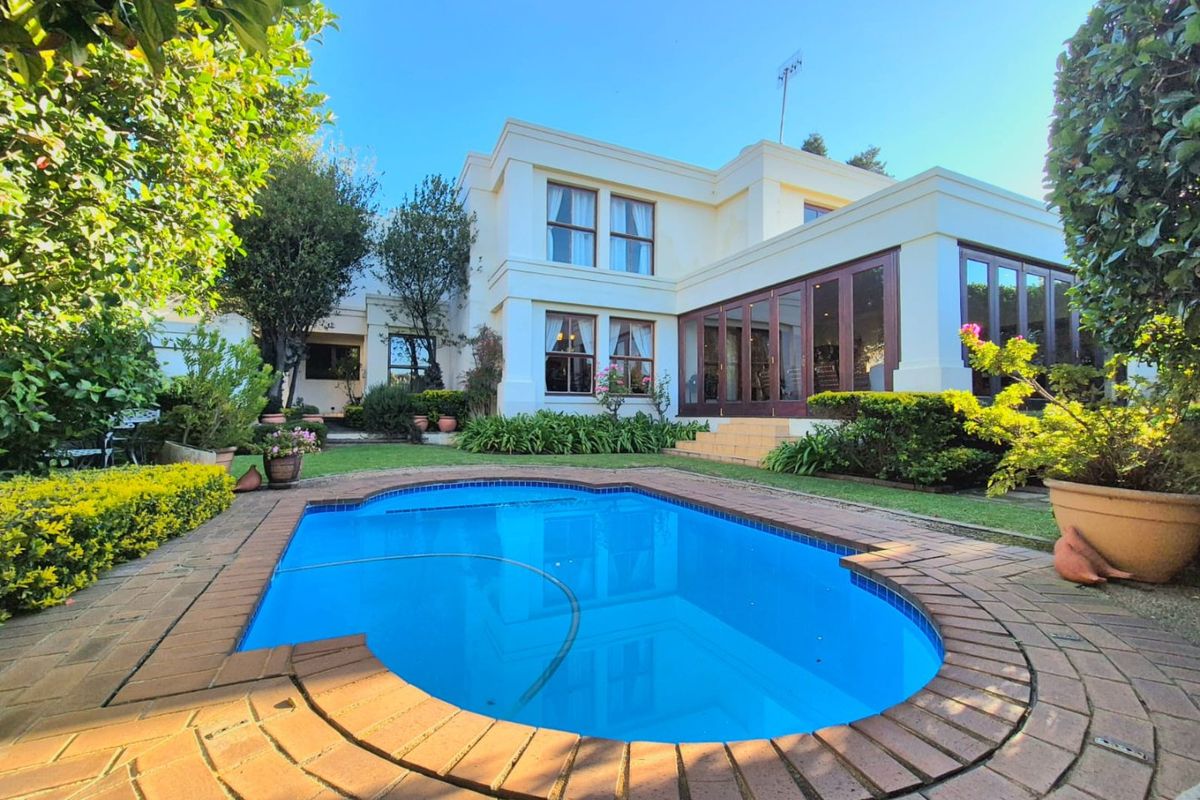 Rear view of the property featuring a well-maintained swimming pool, brick-paved surround, and landscaped garden area with large sliding doors leading into the home.