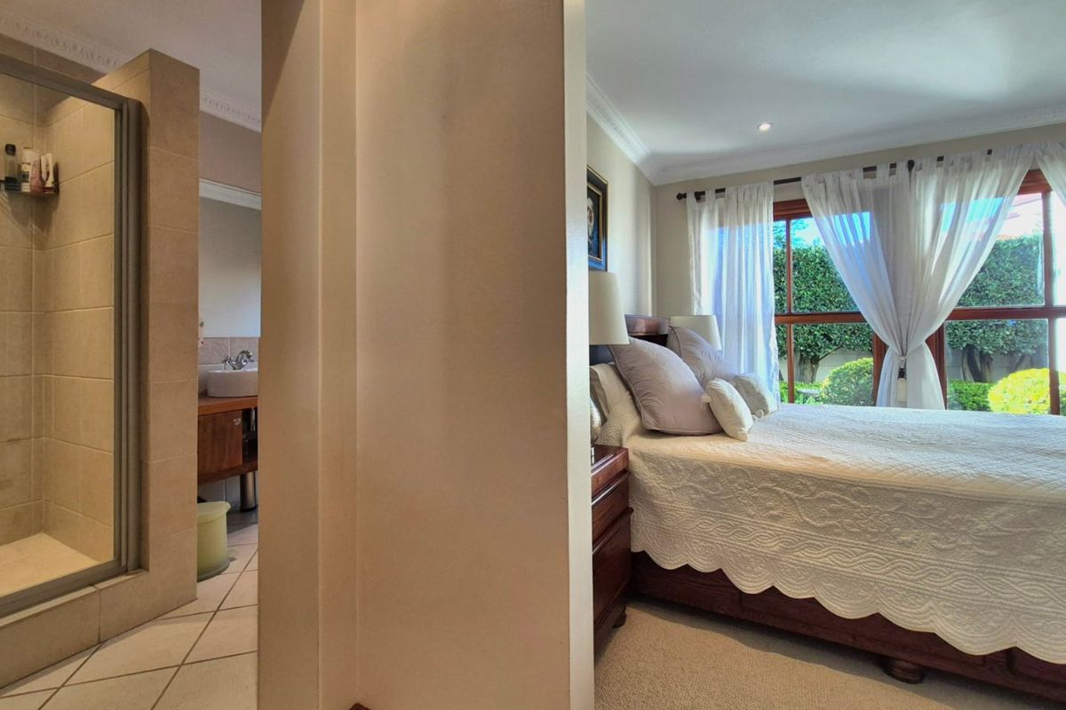 A well-maintained bedroom featuring an integrated en-suite bathroom with a glass shower enclosure, tiled flooring, and neutral finishes throughout.