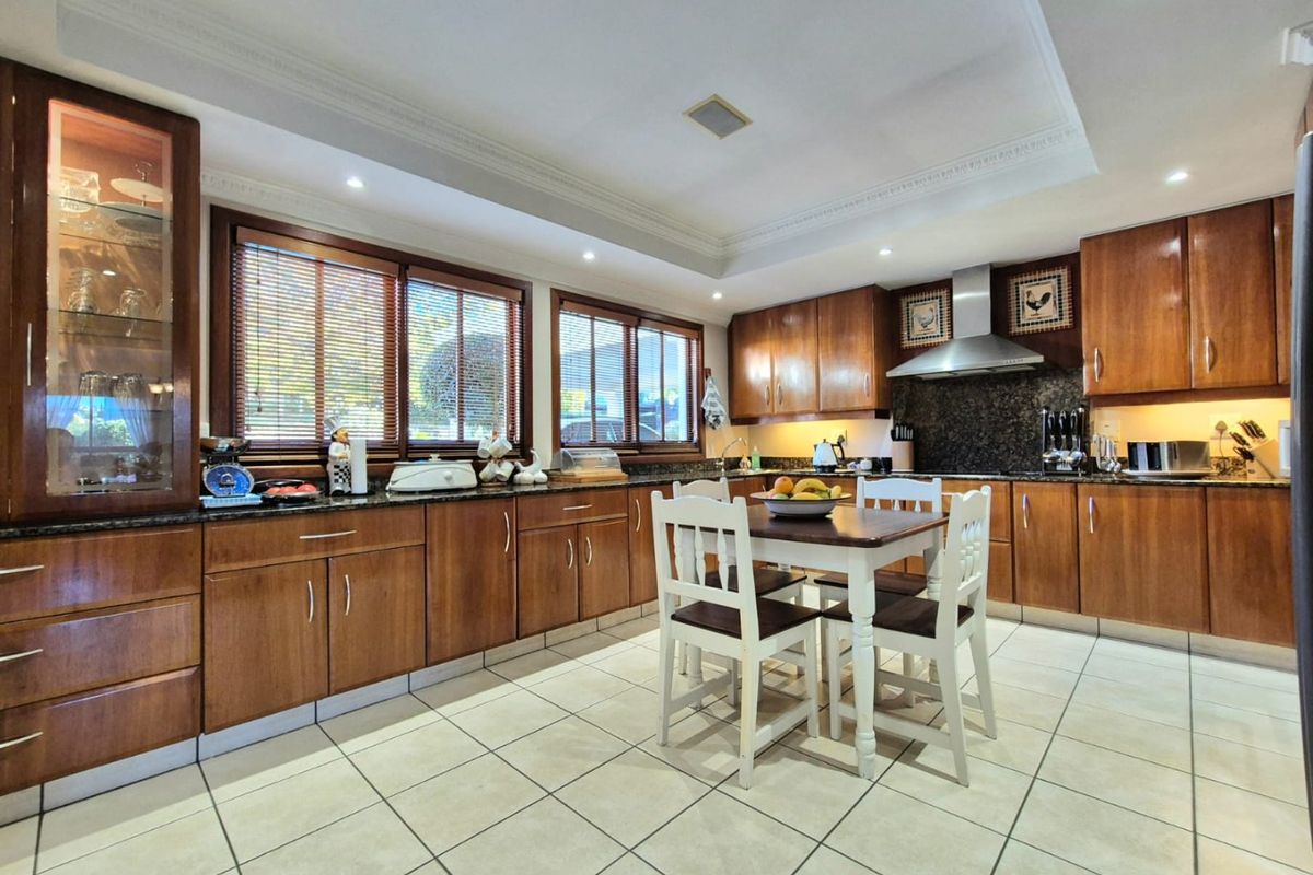 Spacious kitchen featuring warm wooden cabinetry, granite countertops, stainless steel extractor fan, and tiled flooring with integrated recessed lighting.