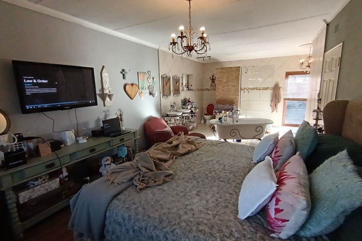 Spacious bedroom featuring an integrated open-plan bathroom with a freestanding bathtub, glass shower, and double vanity, complemented by decorative chandelier lighting.