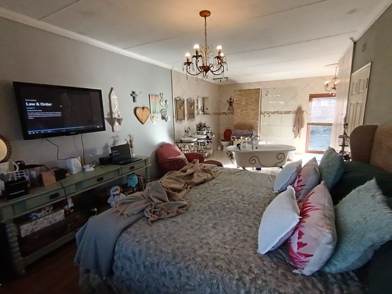 Spacious bedroom featuring an integrated open-plan bathroom with a freestanding bathtub, glass shower, and double vanity, complemented by decorative chandelier lighting.