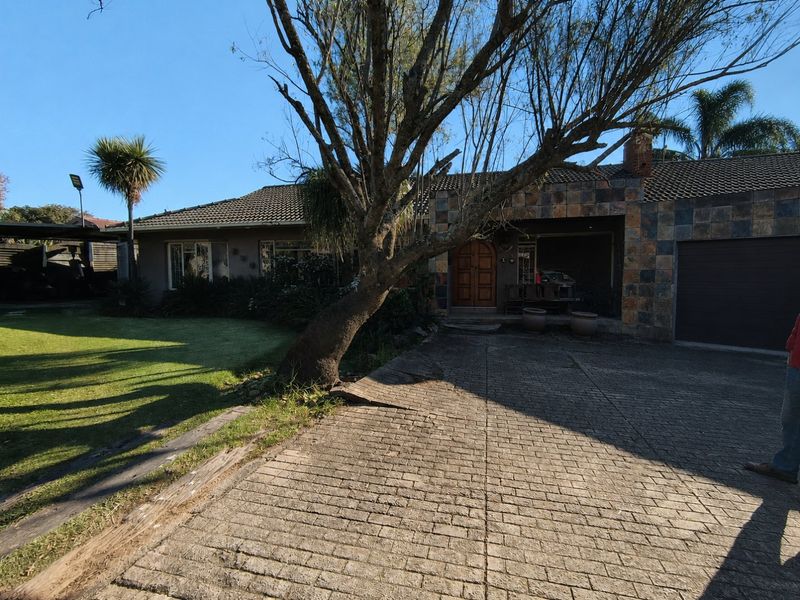 Front elevation of a single-story house featuring a paved driveway, stone-clad facade, tiled roof, and a timber entrance door.