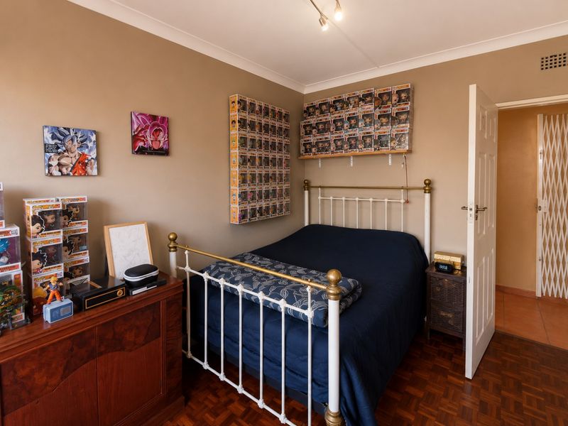 A well-maintained bedroom featuring classic parquet flooring, neutral wall tones, and a ceiling-mounted spotlight track, offering a comfortable and functional living space.