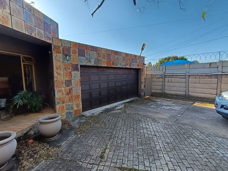 Front exterior view featuring a stone-tiled facade, a sectional garage door, and a paved driveway enclosed by a precast concrete wall with security fencing.