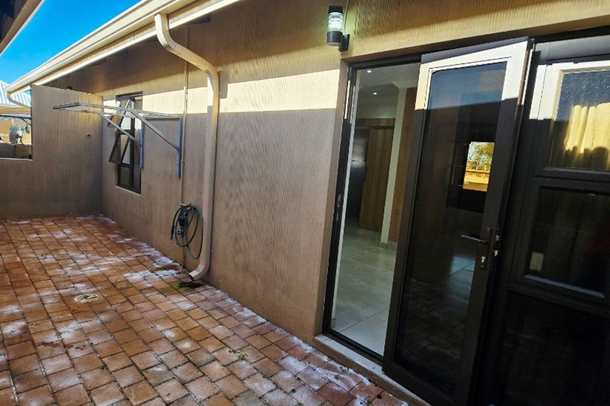 A paved rear courtyard area featuring a wall-mounted clothesline, exterior lighting, and direct access to the interior through a sliding glass door.