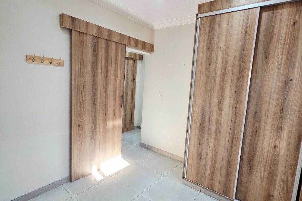 A bright bedroom featuring modern wood-grain sliding wardrobe doors, a matching sliding barn-style door, tiled flooring, and recessed ceiling lighting.