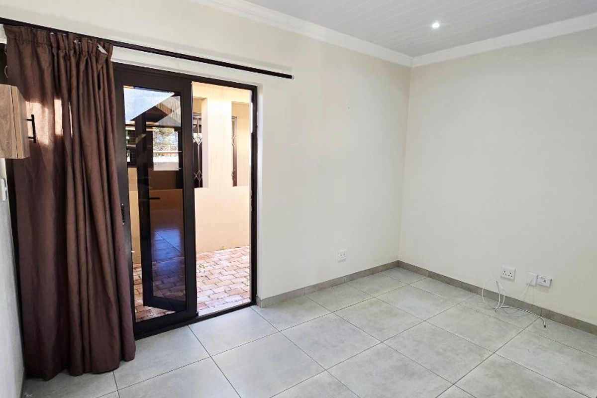 A bright, empty living room featuring neutral floor tiles, recessed ceiling lighting, and a sliding glass door providing access to an outdoor patio area.