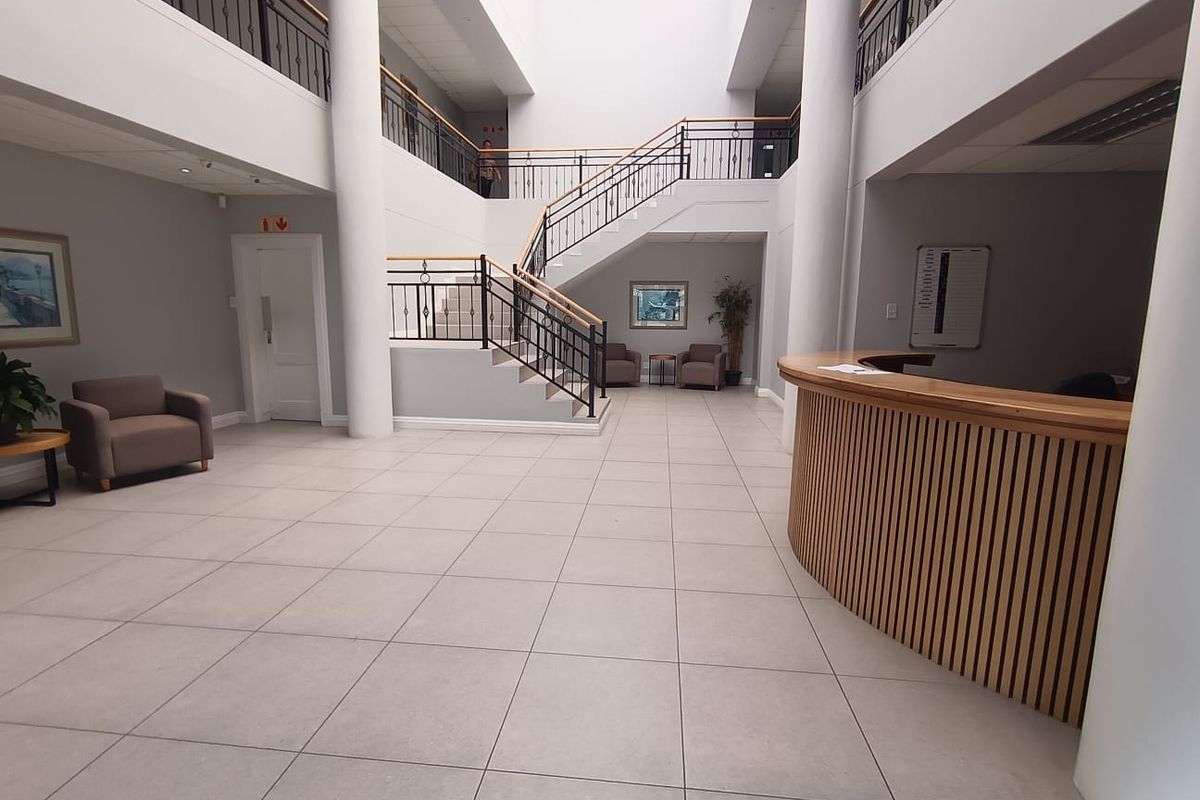 Spacious commercial building entrance featuring a central reception desk, grand staircase with wrought iron balustrades, and a large overhead skylight.