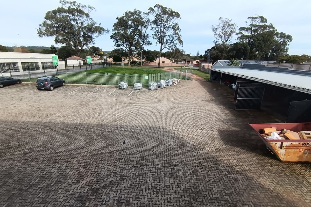 An elevated view of a commercial property featuring a paved parking lot, covered parking bays, and a fenced lawn area.