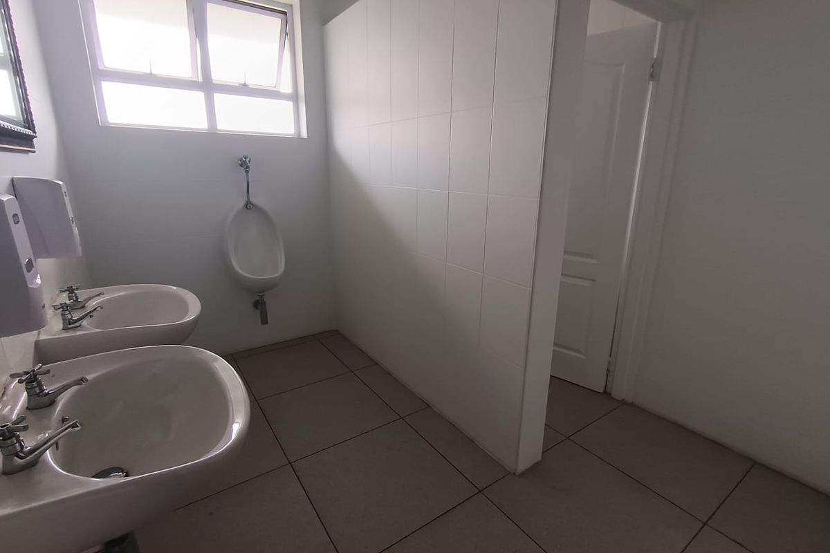 Commercial bathroom facility featuring dual pedestal wash basins, a wall-mounted urinal, tiled flooring, and a privacy partition wall.
