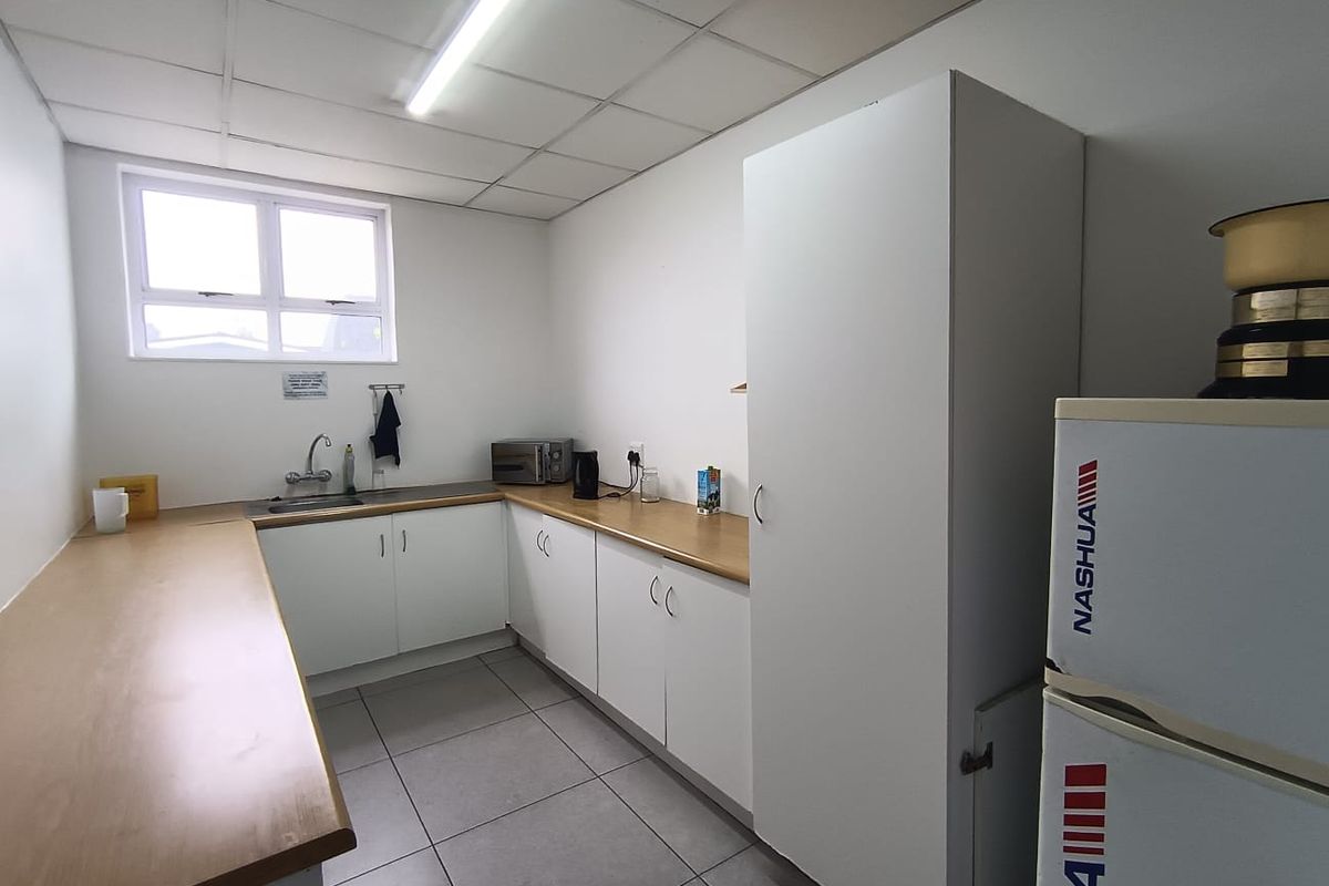 A functional commercial kitchen area featuring laminate countertops, built-in white cabinetry, a stainless steel sink, and tiled flooring under a drop ceiling.