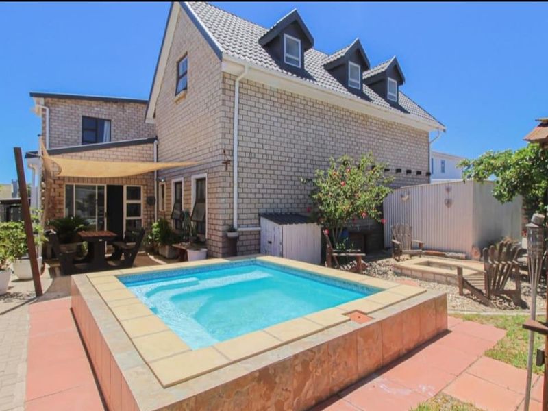 Rear exterior view featuring a raised swimming pool, paved patio area with shade sail, and a multi-story brick house with dormer windows.