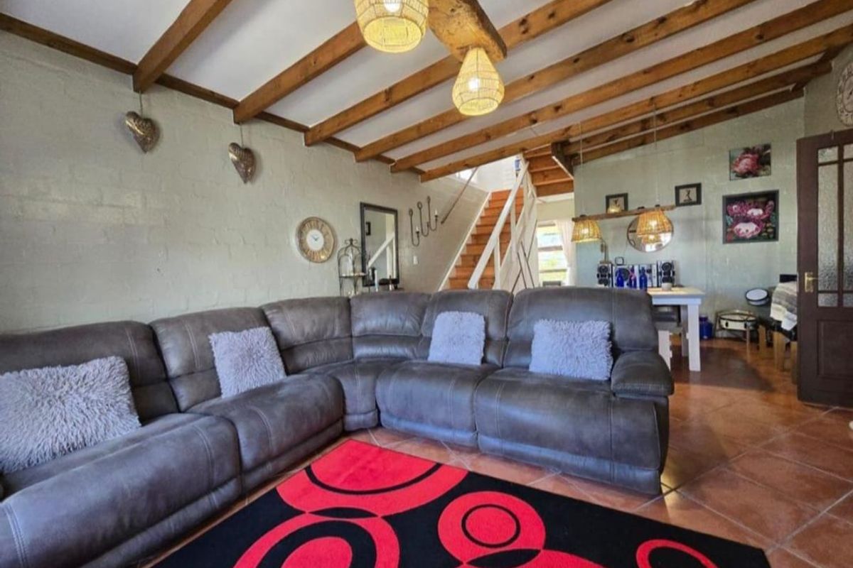 A living room featuring exposed timber ceiling beams, tiled flooring, and an internal staircase leading to the upper level.