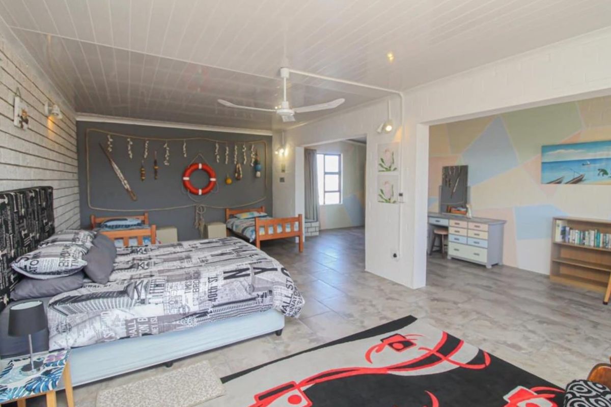 Spacious bedroom featuring tiled flooring, a ceiling fan, and an exposed brick wall, with an adjoining area suitable for a dressing or study space.