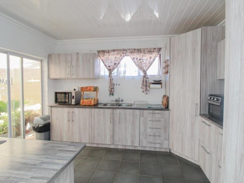 A functional kitchen featuring light wood-grain laminate cabinetry, dark tiled flooring, and direct access to the outdoor area via a sliding glass door.