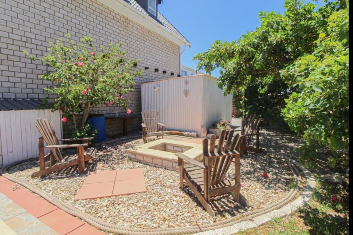 A rear garden area featuring a built-in stone fire pit, gravel landscaping, and a corrugated metal storage shed adjacent to the main house structure.