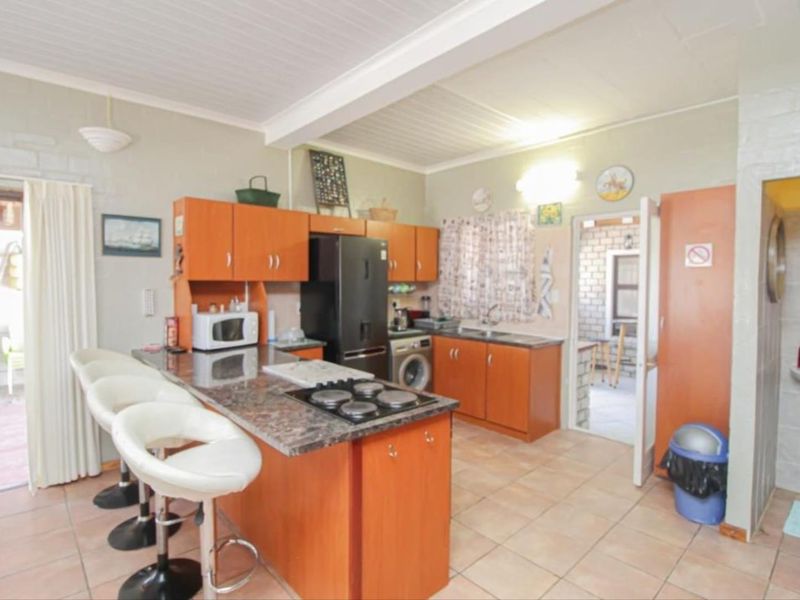 A functional kitchen featuring wooden cabinetry, granite countertops, a built-in hob, and tiled flooring, with an open-plan layout connecting to adjacent living spaces.