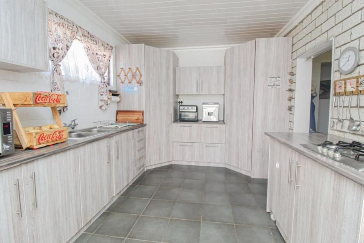 A functional kitchen featuring light wood-grain cabinetry, laminate countertops, a double bowl sink, and a built-in gas hob with tiled flooring.