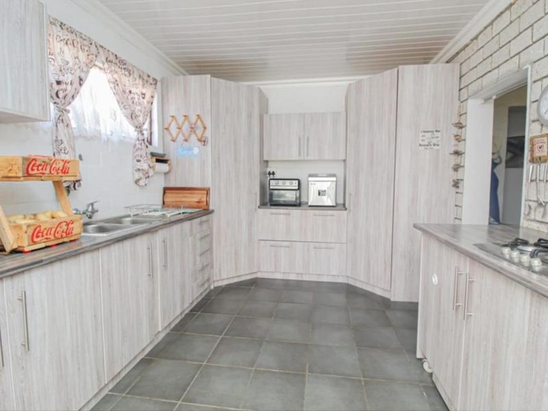 A functional kitchen featuring light wood-grain cabinetry, laminate countertops, a double bowl sink, and a built-in gas hob with tiled flooring.