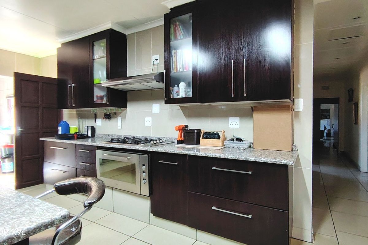 A functional kitchen featuring dark wood cabinetry, granite countertops, a built-in oven with gas hob, and tiled finishes throughout.
