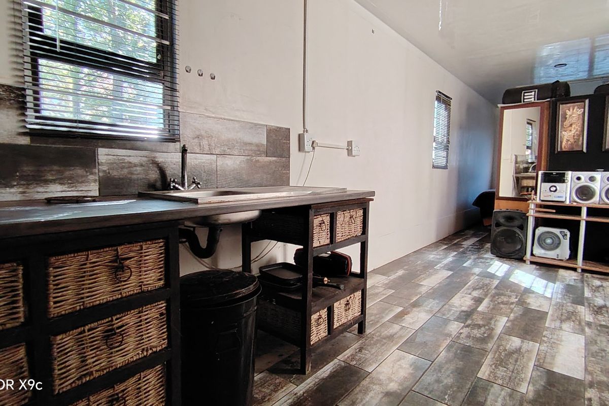 A rustic-style kitchen area featuring wood-look floor tiles, a stainless steel sink, and a tiled backsplash, requiring some finishing touches to the walls and wiring.