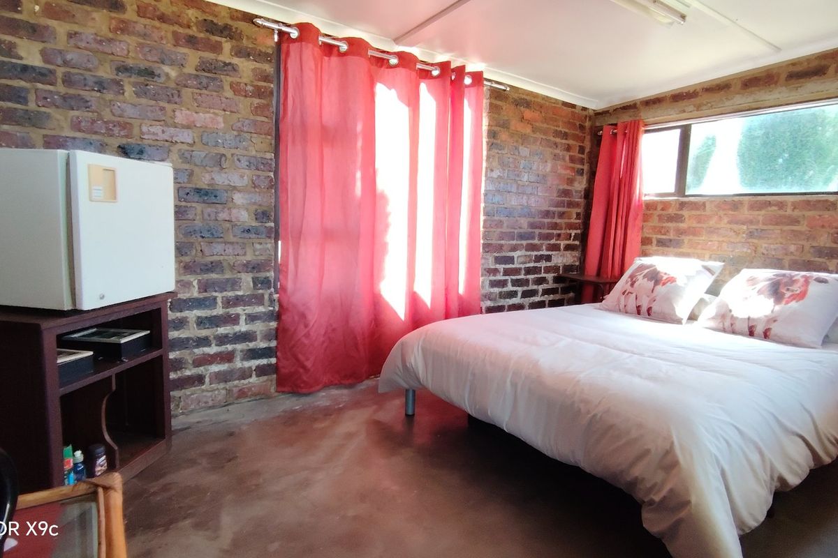 A rustic bedroom featuring exposed brick walls, concrete flooring, and large windows, offering a unique industrial-farm aesthetic.
