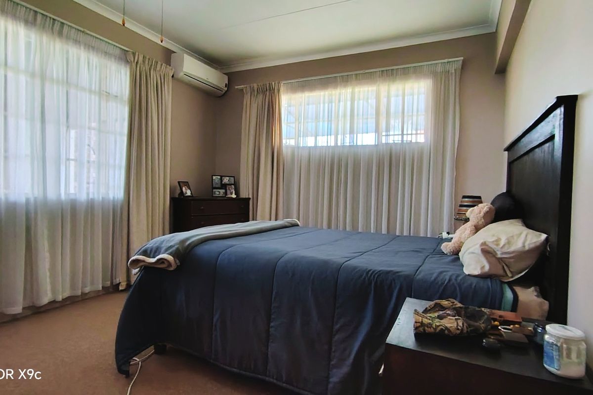 A well-lit bedroom featuring neutral wall tones, carpeted flooring, and a wall-mounted air conditioning unit.