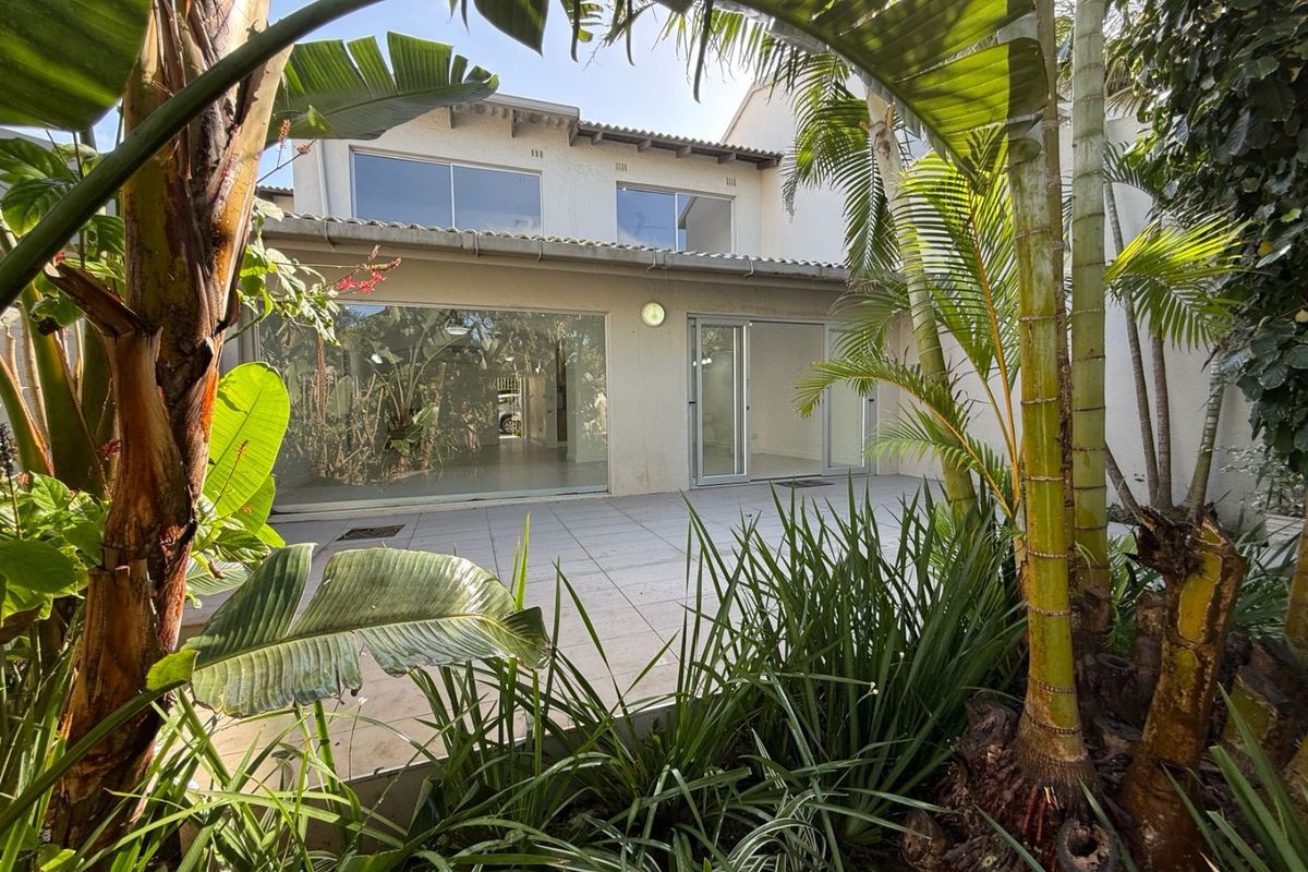 Rear view of the townhouse featuring a paved patio area, large sliding glass doors, and established garden foliage.