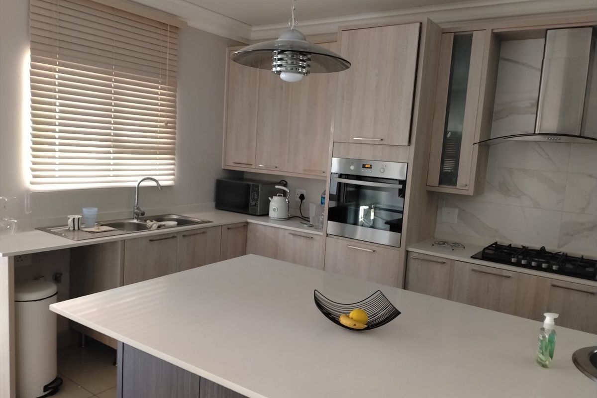 Modern kitchen featuring light wood cabinetry, stone countertops, a central island, built-in oven, gas hob, and stainless steel extractor fan.
