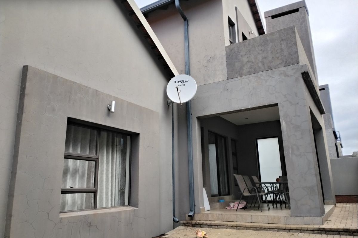 Rear view of the townhouse featuring a covered patio area, paved terrace, and exterior plaster finish with visible hairline cracking.