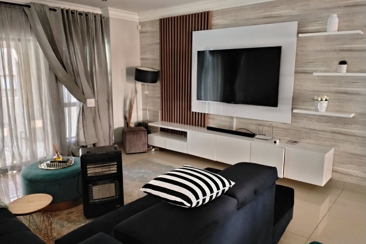 Modern living room featuring a custom media wall with slatted timber accents, floating shelving, and sleek white cabinetry, complemented by large sliding glass doors.