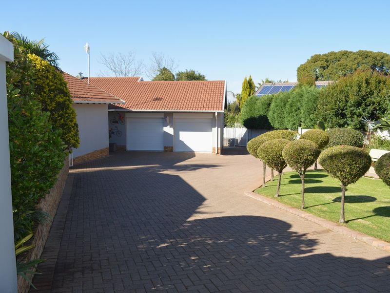 A well-maintained front exterior featuring a paved driveway leading to a double garage, complemented by a neat garden and boundary wall.