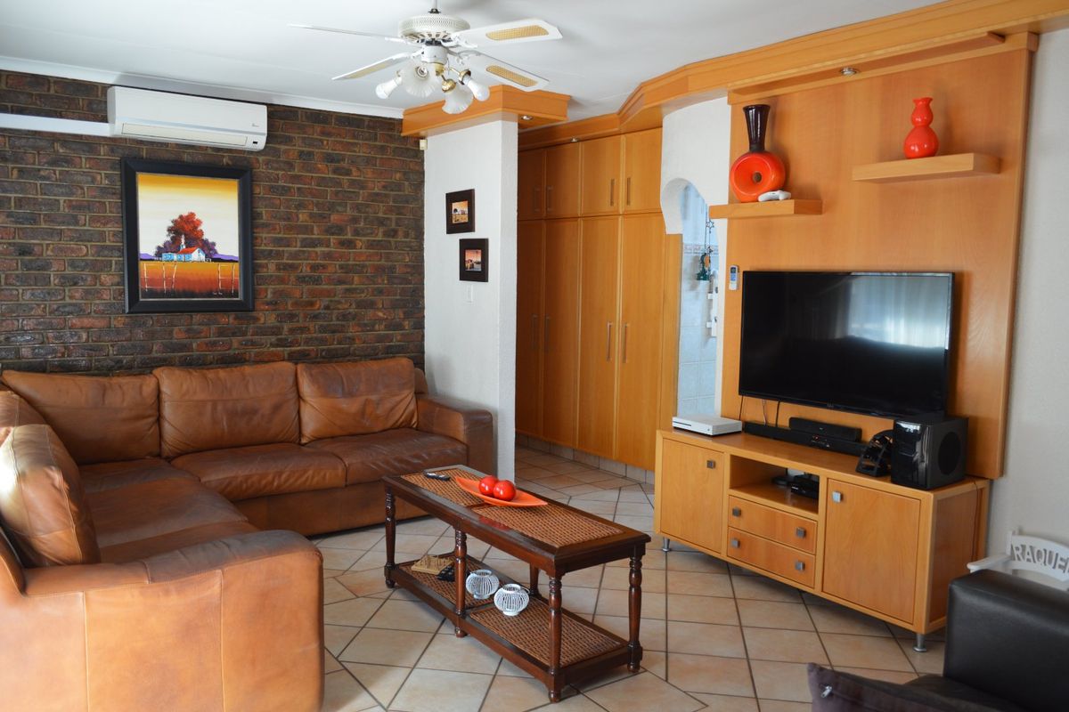 A living room featuring an exposed brick wall, tiled flooring, built-in wooden cabinetry, and a ceiling fan with an integrated air conditioning unit.