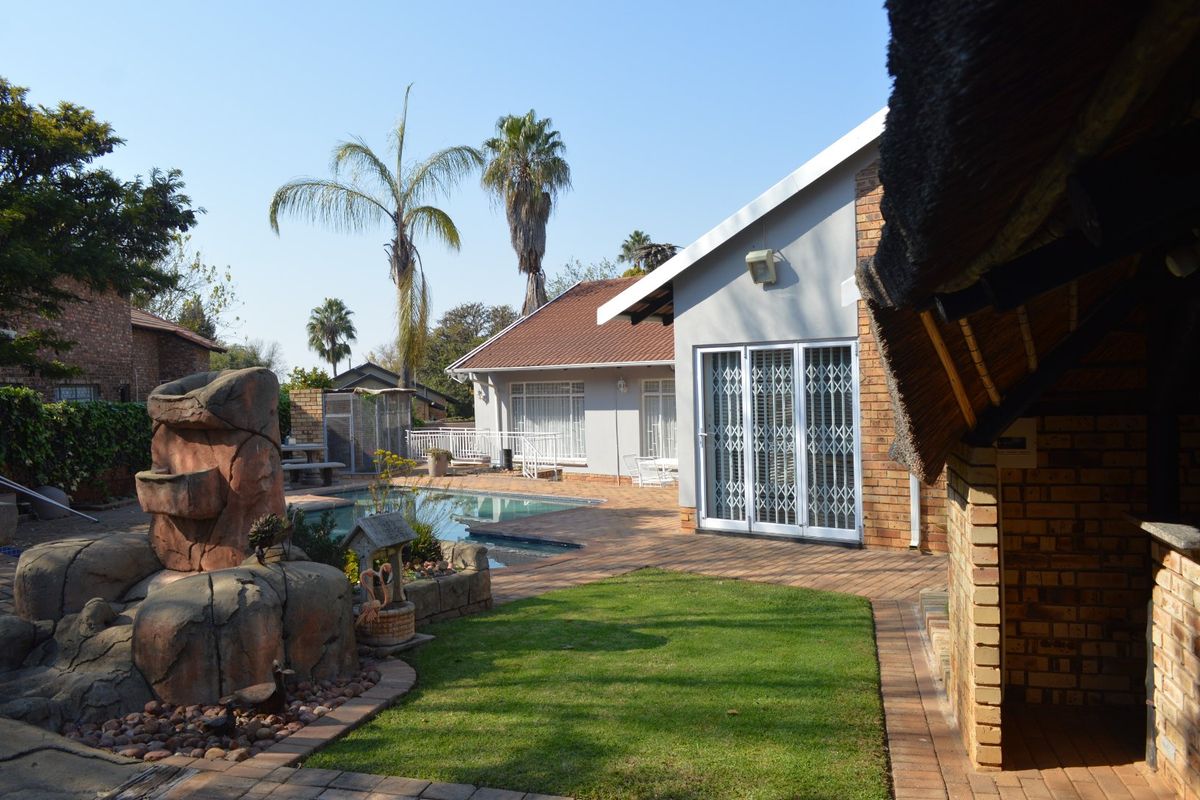 Rear exterior view featuring a swimming pool, paved patio area, landscaped garden, and a covered thatched entertainment space.
