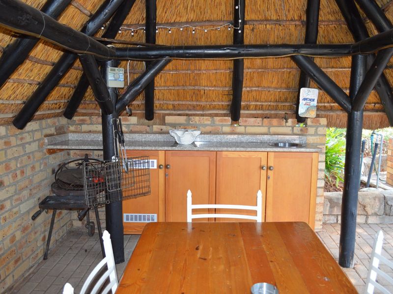 Covered outdoor patio area featuring a traditional thatch roof, exposed timber beams, built-in cabinetry with granite countertops, and a dedicated braai area.