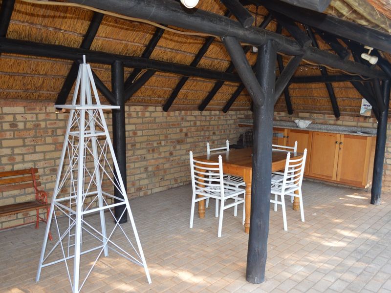 Covered outdoor patio area featuring a traditional thatched roof, exposed timber support beams, brick walls, and built-in cabinetry with a stone countertop.