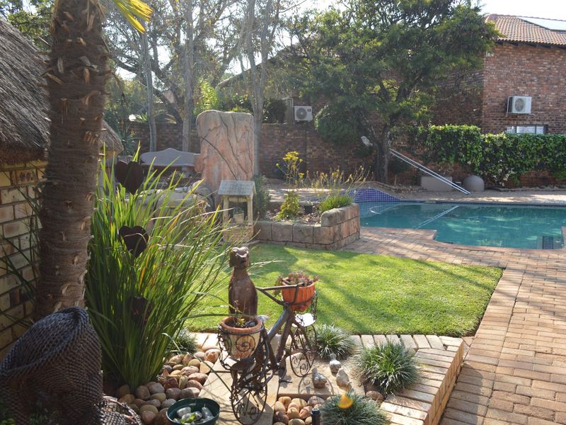 Outdoor pool area featuring a swimming pool, brick paving, and a thatched roof structure set within a landscaped garden with brick boundary walls.