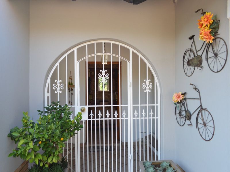 A secure, arched metal gate leads into the main entrance of the home, featuring clean finishes and a welcoming recessed porch area.