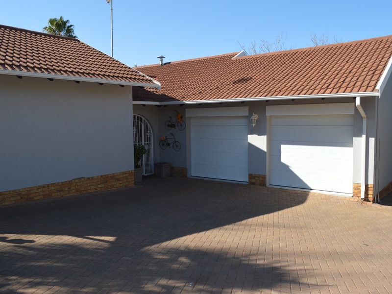 Front view of the property featuring a double garage with white doors, a tiled roof, and a paved driveway.