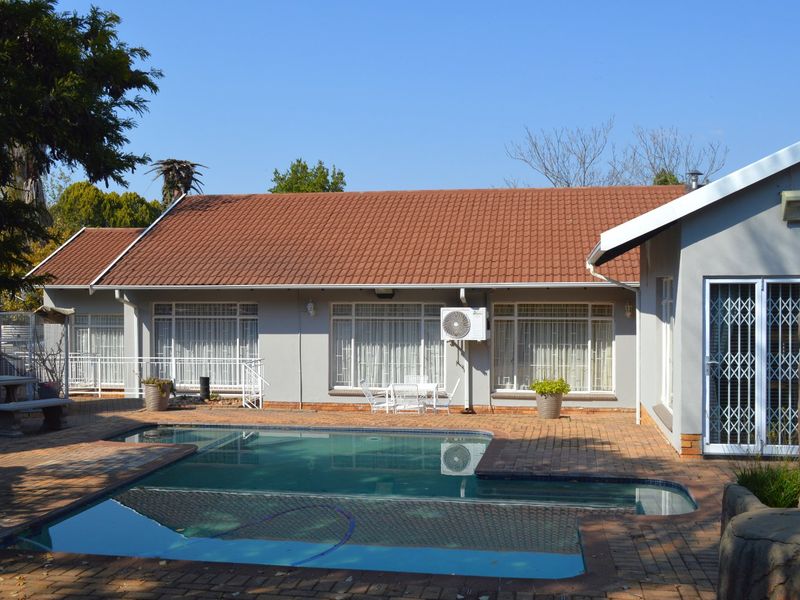 Rear exterior view featuring a swimming pool, brick-paved patio area, and a well-maintained single-story building with a tiled roof.